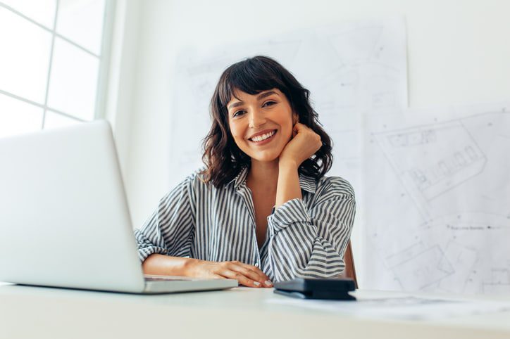 Close up of a smiling female entrepreneur. Businesswoman sitting at her desk working on laptop.